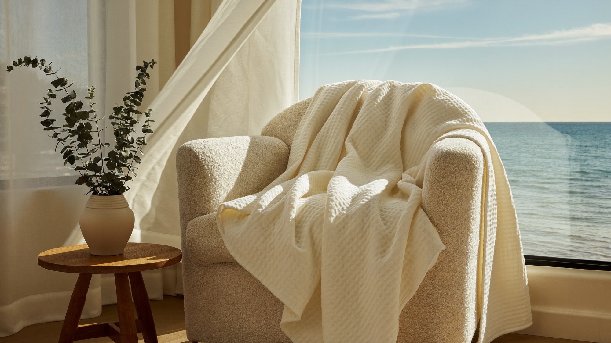 Cream muslin blanket draped over an armchair beside an open window with sheer curtains